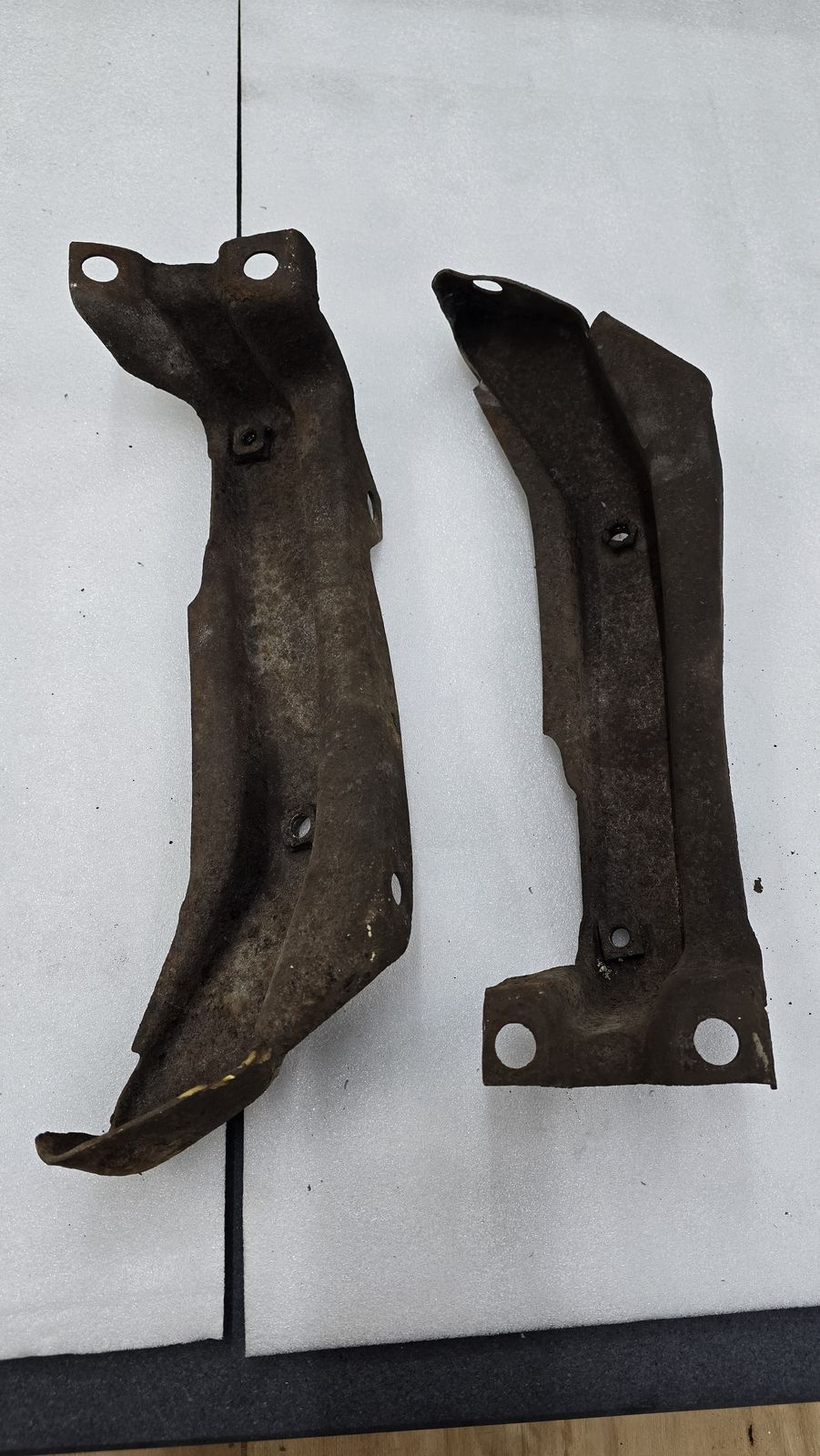 Two heavily corroded steel mounting brackets before cleaning